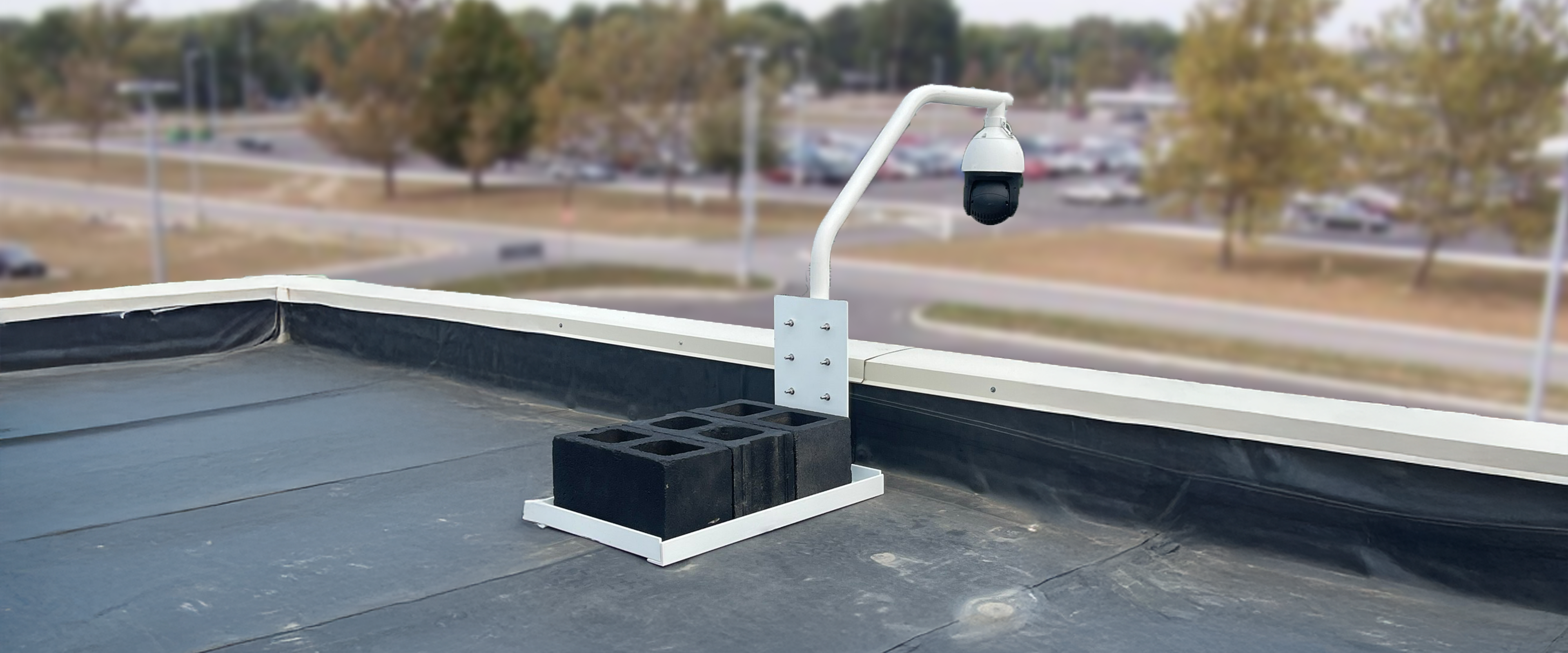 Security camera on a rooftop with a blurred background of trees and buildings.